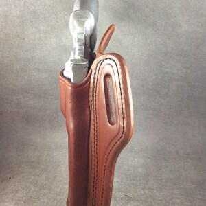 May include: A brown leather holster with a stitched design. The holster is empty and has a metal clip on the back.