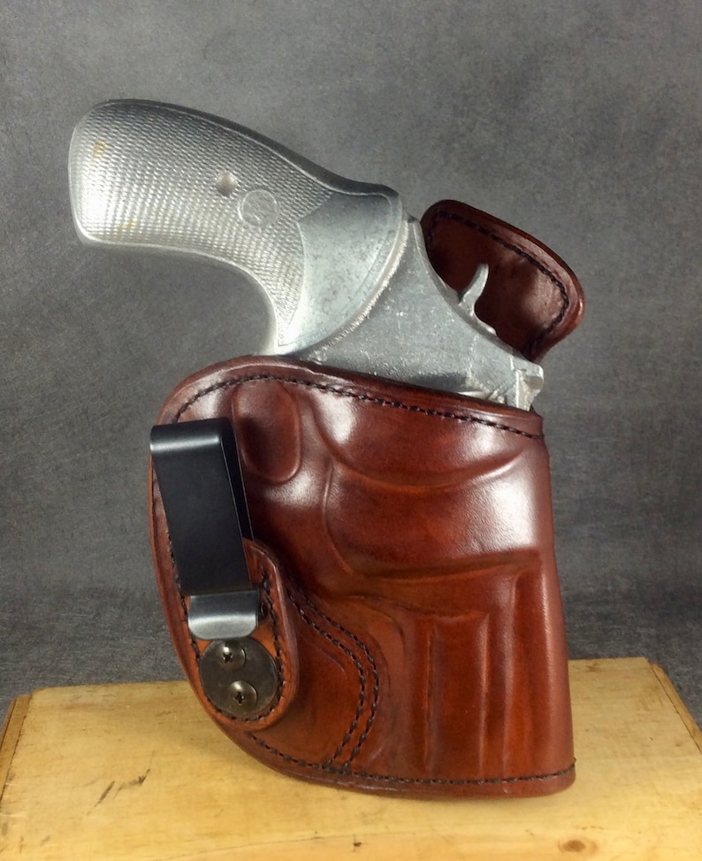 May include: A brown leather holster with a black clip for a small silver handgun.