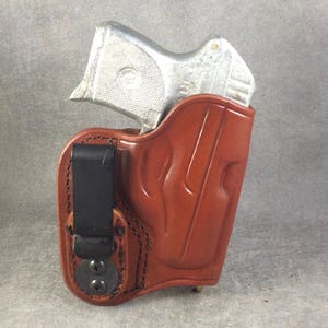May include: A brown leather holster with a flame design and a black clip. A silver handgun is inside the holster.