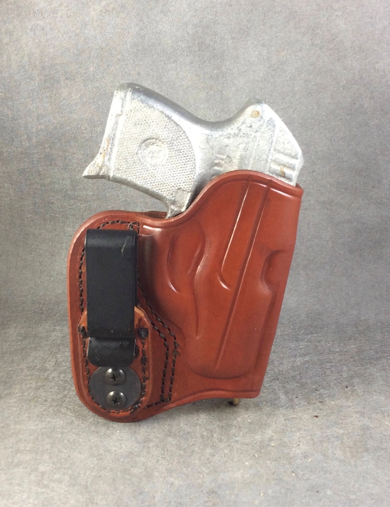 May include: A brown leather holster with a flame design and a black clip. A silver handgun is inside the holster.