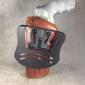 May include: A brown leather holster with a black plastic attachment for a gun. The holster has the text "Blade-Tech" printed on it.