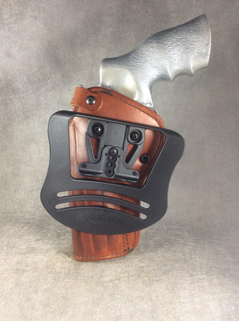 May include: A brown leather holster with a black plastic attachment for a gun. The holster has the text "Blade-Tech" printed on it.