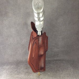 May include: A brown leather holster with a silver gun inside. The holster is designed to be worn on a belt.