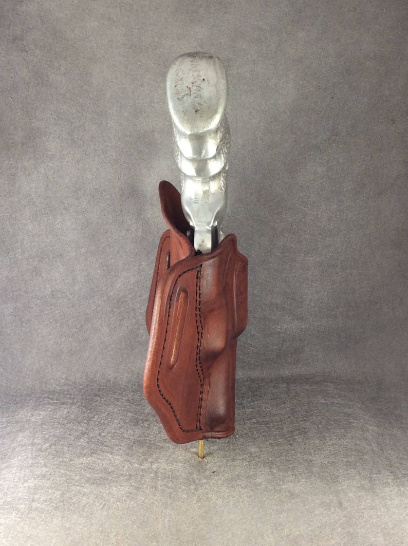 May include: A brown leather holster with a silver gun inside. The holster is designed to be worn on a belt.