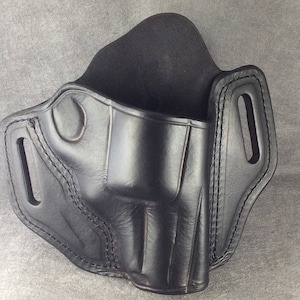 May include: Black leather holster with stitching detail. The holster has a belt loop and a trigger guard.