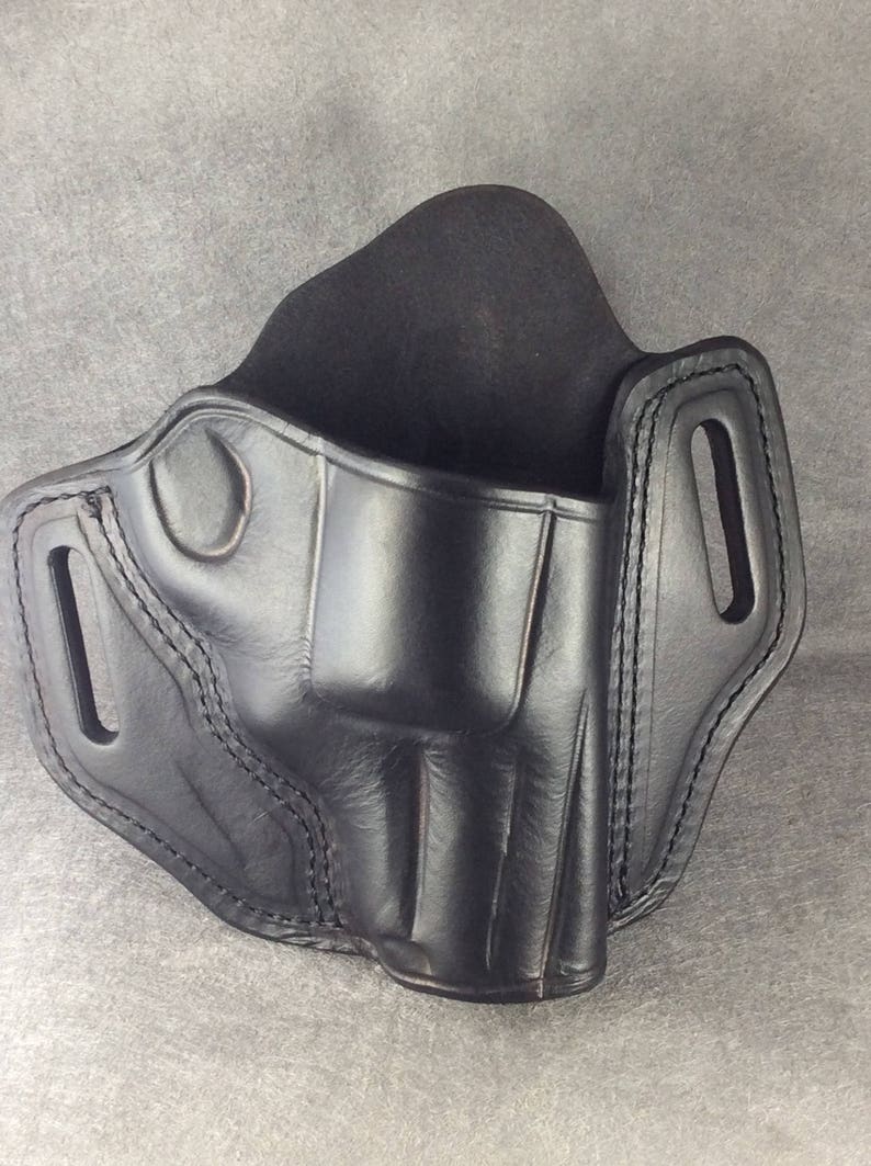 May include: Black leather holster with stitching detail. The holster has a belt loop and a trigger guard.