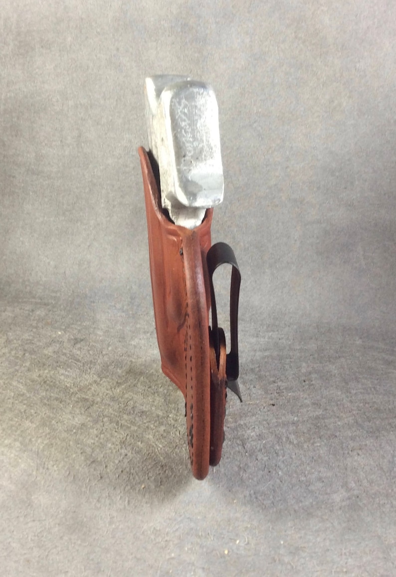 May include: A brown leather holster with a silver metal object inside. The holster has a black belt clip.