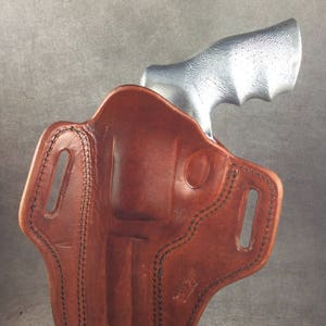 May include: A brown leather holster with a stitched design. The holster is designed to hold a revolver with a silver finish.