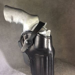 May include: A black leather holster with a strap for a silver revolver.