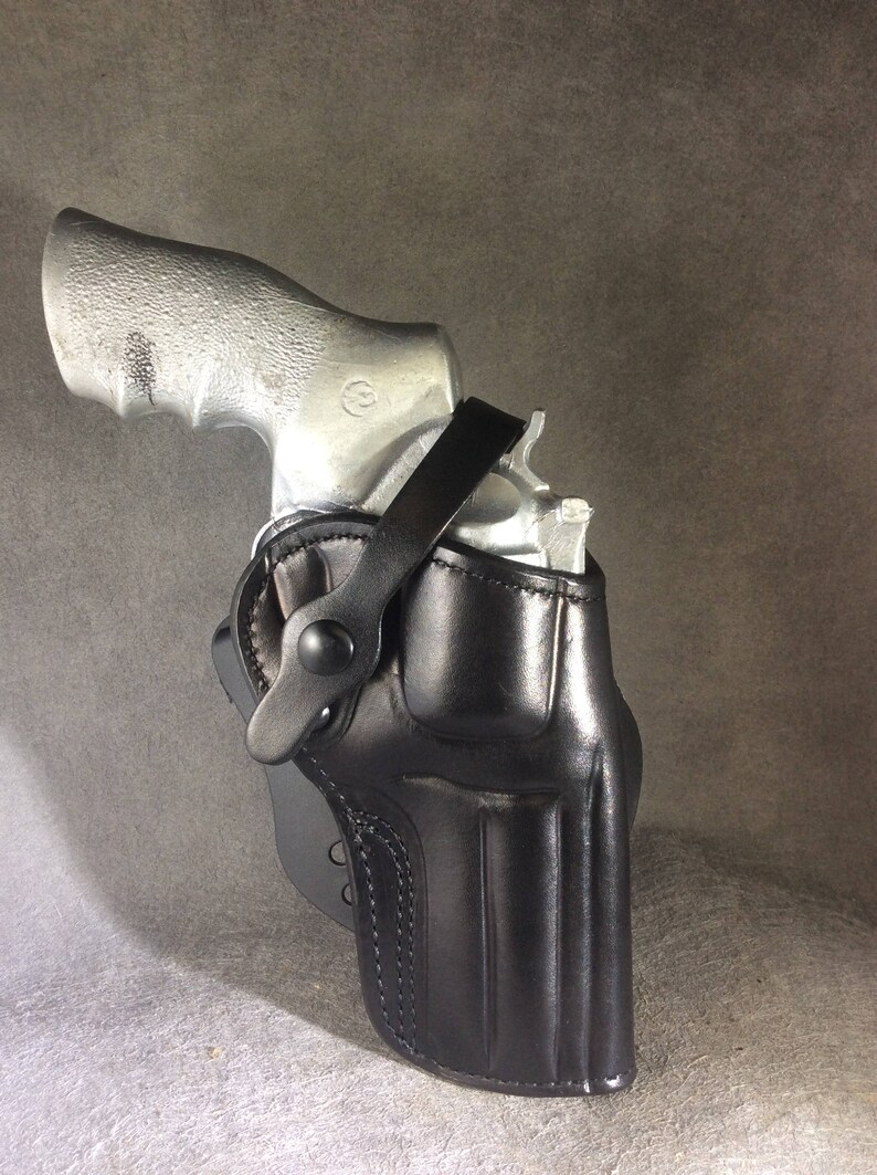 May include: A black leather holster with a strap for a silver revolver.