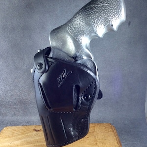 May include: A black leather holster with a silver revolver inside. The holster has a belt loop and a snap closure. The revolver has a silver finish and a black grip.