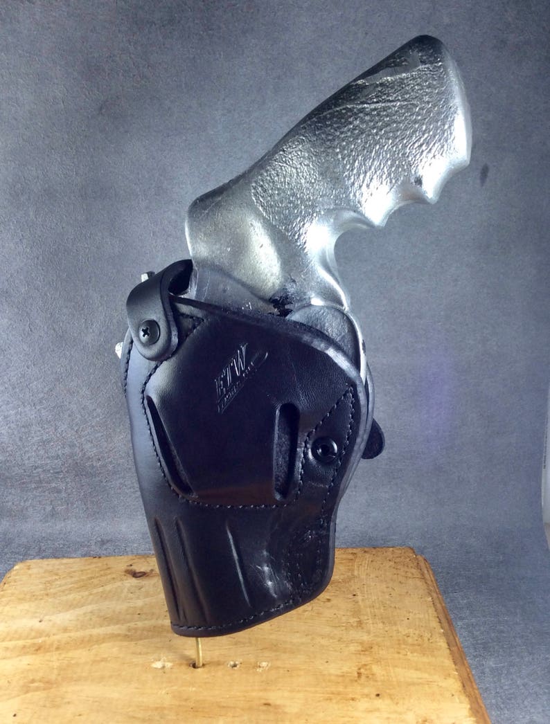 May include: A black leather holster with a silver revolver inside. The holster has a belt loop and a snap closure. The revolver has a silver finish and a black grip.