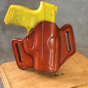 May include: A brown leather holster with a yellow plastic gun inside. The holster has a belt loop and is designed for concealed carry.