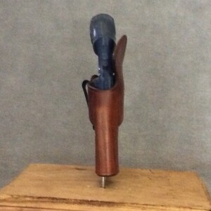 May include: A brown leather holster for a handgun, displayed on a wooden base.