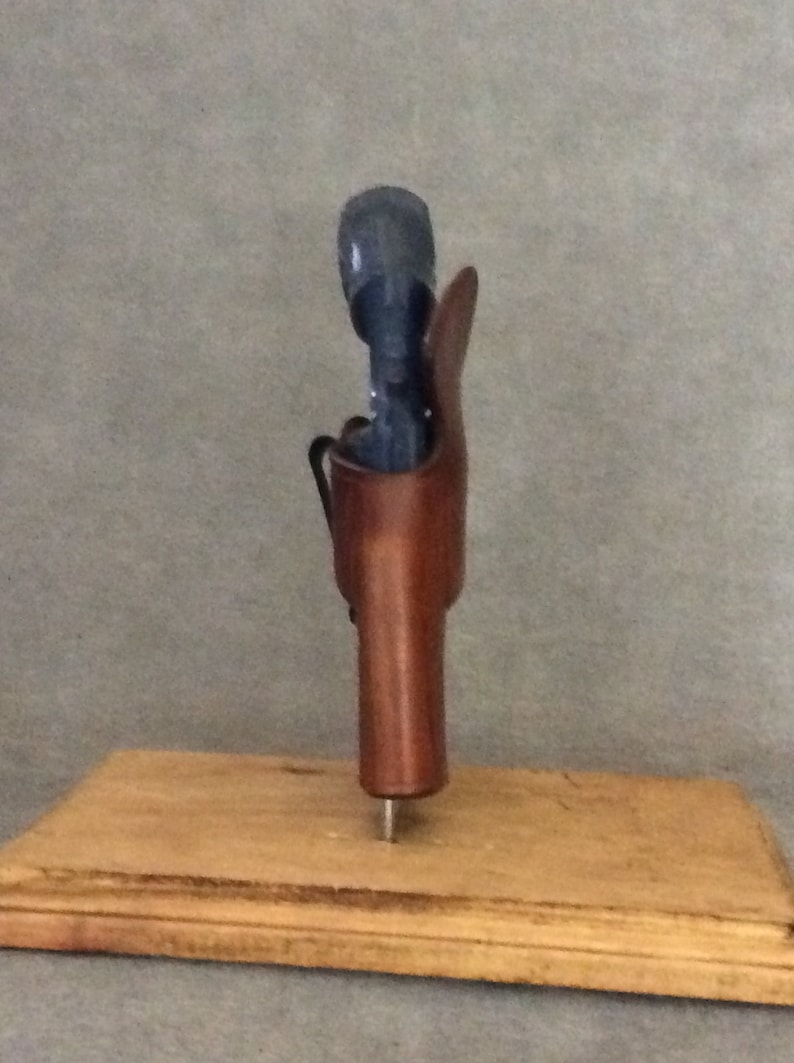 May include: A brown leather holster for a handgun, displayed on a wooden base.