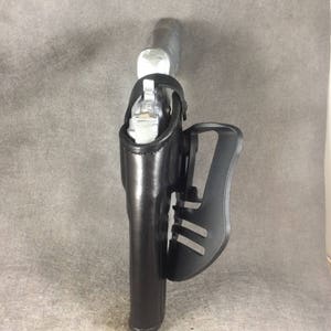 May include: A black leather holster with a silver gun inside. The holster has a black plastic clip on the side.