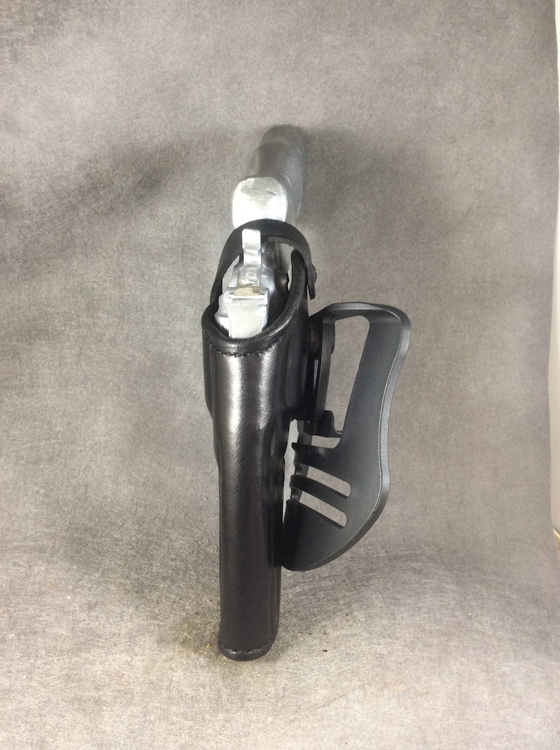 May include: A black leather holster with a silver gun inside. The holster has a black plastic clip on the side.
