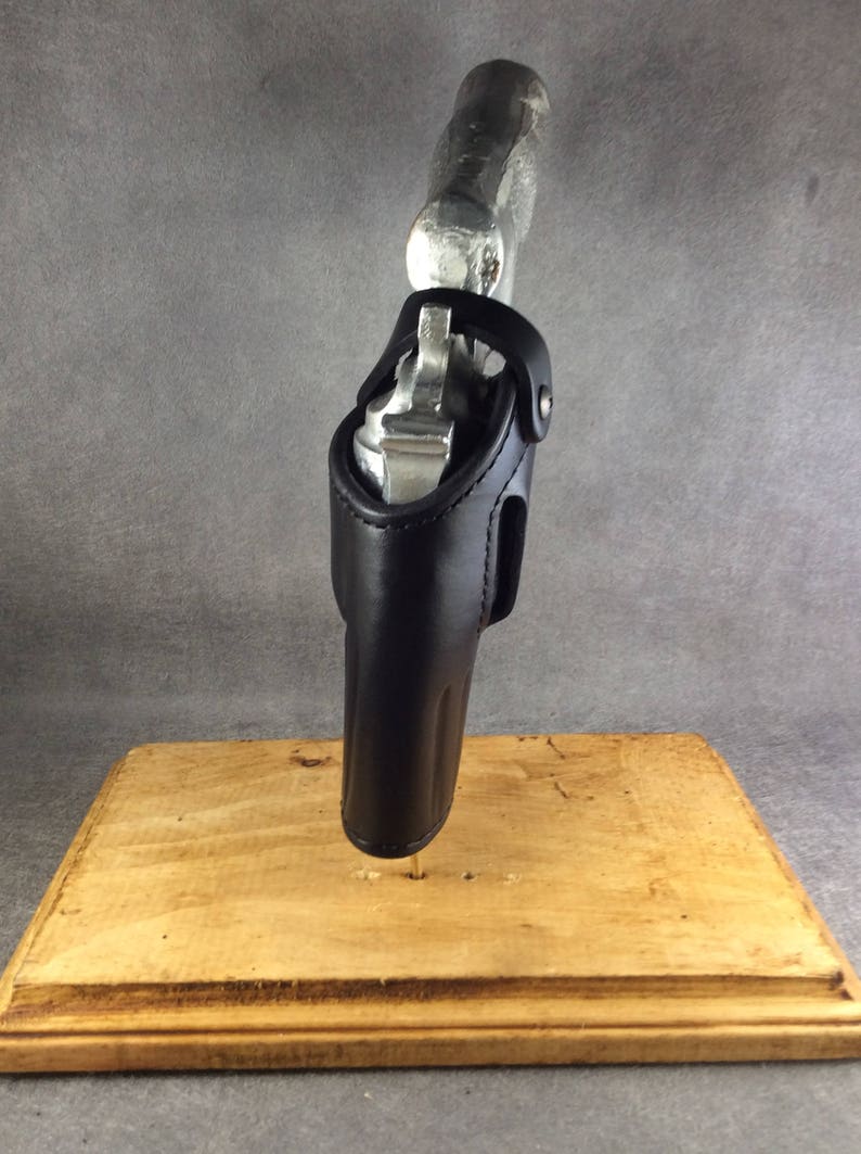May include: A black leather holster for a silver revolver. The holster is designed to be worn on the hip and has a belt loop. The revolver is partially visible in the holster.