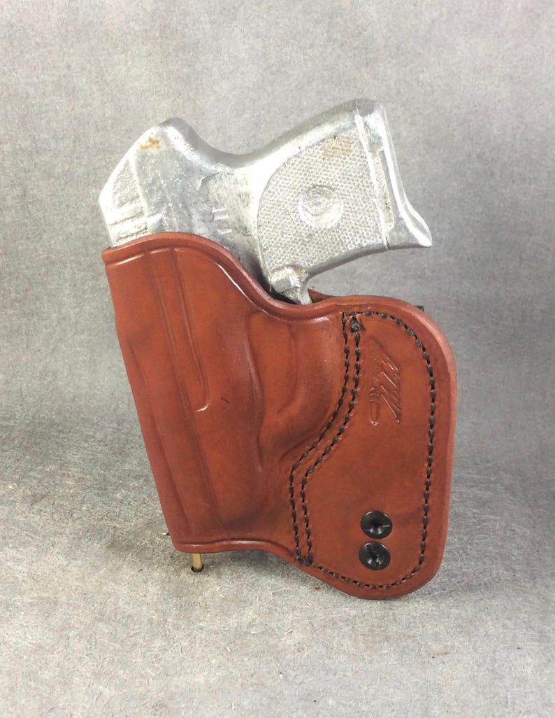 May include: A brown leather holster with a silver handgun inside. The holster has a stitched design and two black snaps.