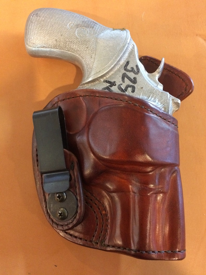 May include: A brown leather holster with a silver handgun inside. The holster has a clip on the side and the gun has the number "322" written on it.
