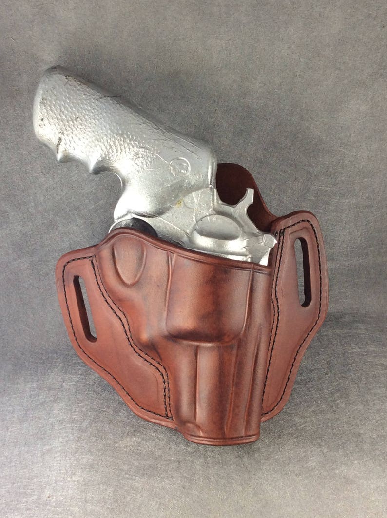 May include: A brown leather holster for a silver revolver. The holster has a belt loop and a strap to secure the gun.