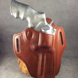 May include: A brown leather holster with a silver revolver inside. The holster has a belt loop and a flap that covers the trigger guard.