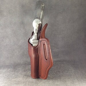 May include: A brown leather holster for a handgun. The holster has a stitched design and a flap that covers the top of the gun.