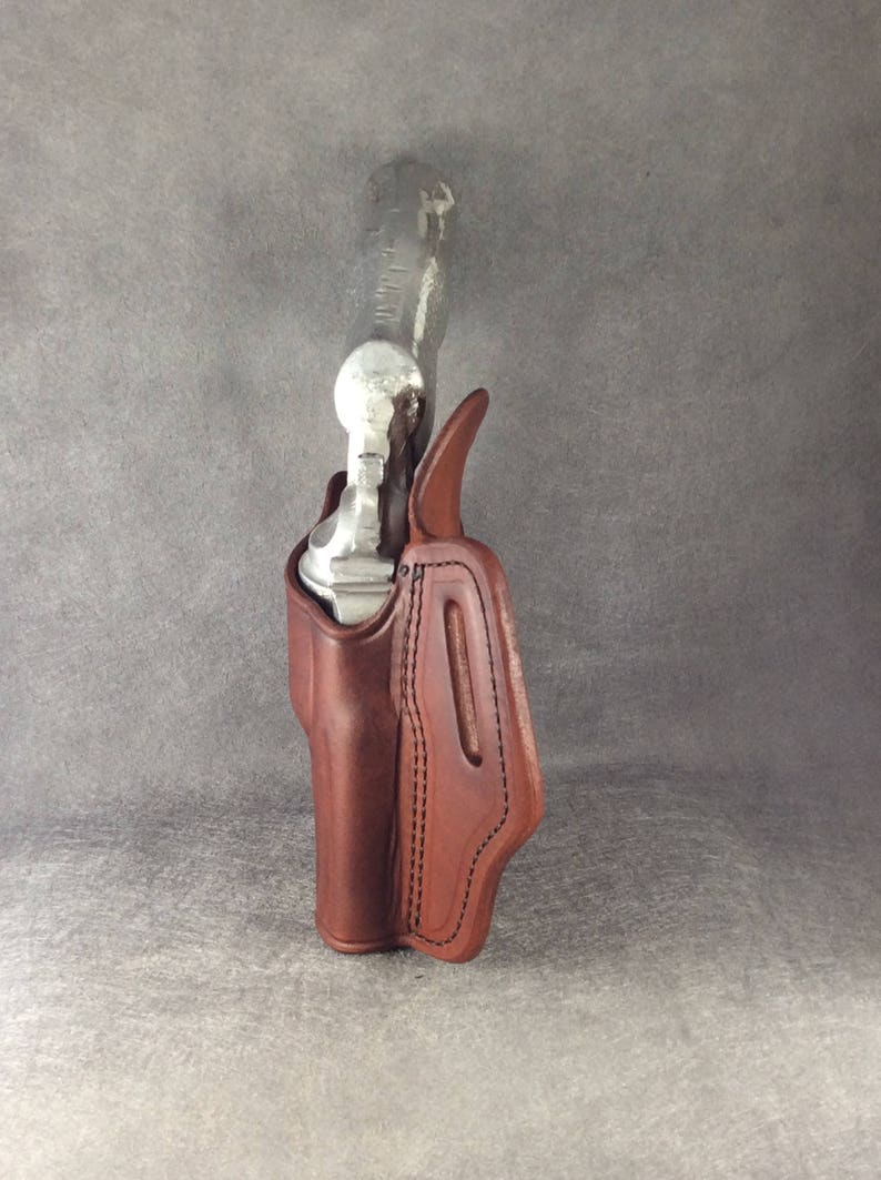 May include: A brown leather holster for a handgun. The holster has a stitched design and a flap that covers the top of the gun.