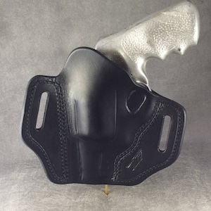 May include: A black leather holster with a silver revolver inside. The holster has a belt loop and a snap closure.