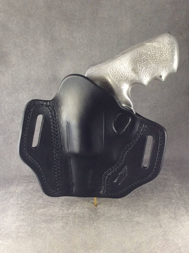 May include: A black leather holster with a silver revolver inside. The holster has a belt loop and a snap closure.