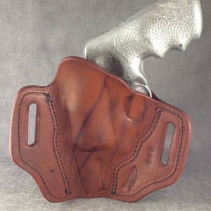 May include: A brown leather holster with a stitched design and a belt loop. The holster is designed to hold a silver revolver.