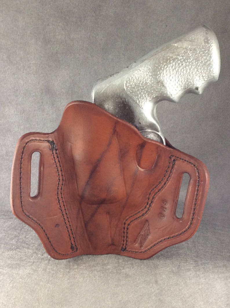 May include: A brown leather holster with a stitched design and a belt loop. The holster is designed to hold a silver revolver.