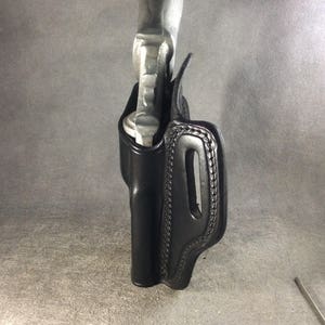 May include: A black leather holster for a small handgun. The holster has a stitched design and a belt loop.