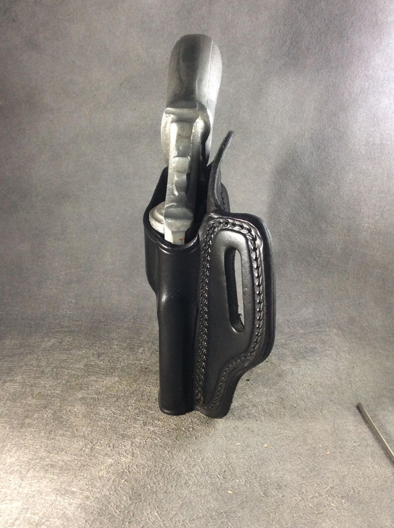 May include: A black leather holster for a small handgun. The holster has a stitched design and a belt loop.