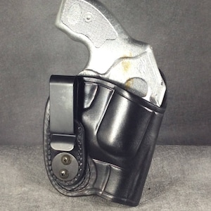 May include: A black leather holster with a clip for carrying a small silver handgun.