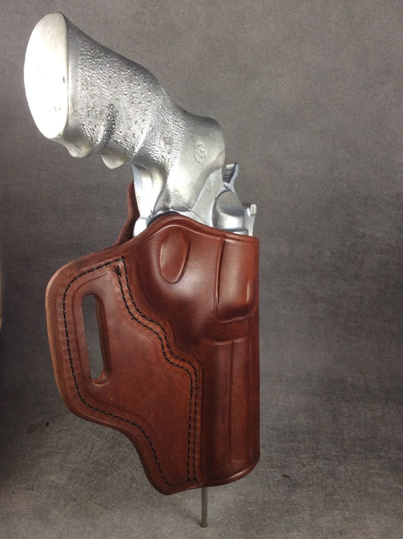 May include: A brown leather holster with a silver revolver inside. The holster has a belt loop and a stitched design.