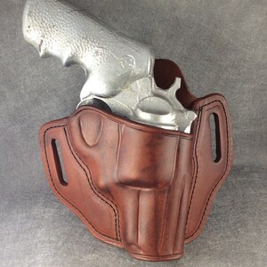 May include: A brown leather holster for a silver revolver. The holster has a belt loop and a snap closure.