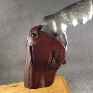 May include: A brown leather holster for a silver revolver. The holster has a snap closure and is designed to fit snugly around the gun.