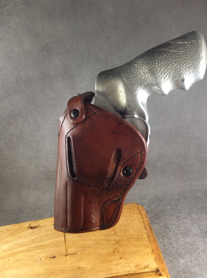 May include: A brown leather holster for a silver revolver. The holster has a snap closure and is designed to fit snugly around the gun.