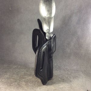 May include: A black leather holster with a silver metal gun inside.