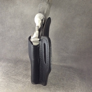 May include: A black leather holster for a handgun. The holster has a stitched design and a belt loop.