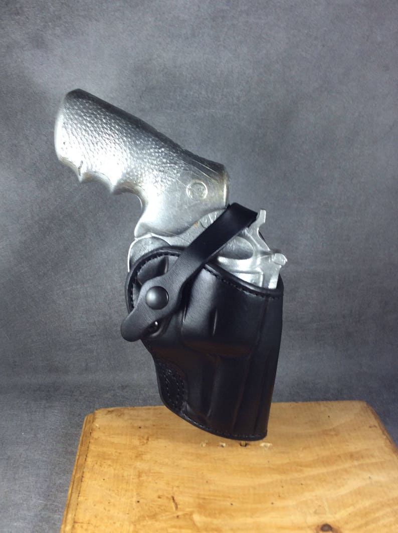 May include: A black leather holster with a strap for a silver revolver.