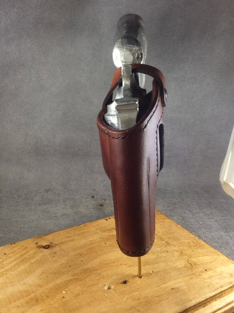 May include: A brown leather holster for a silver handgun. The holster is mounted on a wooden stand.