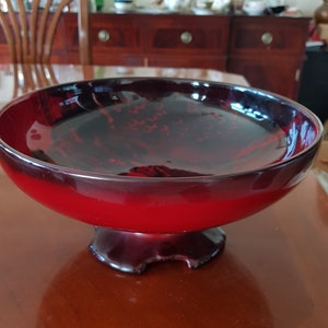May include: A red and black ceramic bowl with a wide, round base and a flared lip. The bowl has a glossy finish and a decorative pattern.