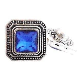 May include: A pair of silver cufflinks with a blue square gemstone in the center. The cufflinks have a decorative border.