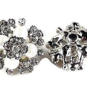 May include: Two silver tone earrings. One earring is a cluster of small white pearls and rhinestones. The other earring is a more abstract design with a silver tone finish.