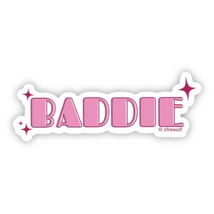 May include: Pink sticker with the word "BADDIE" in a retro font with pink stars. The text "© shewolf" is at the bottom of the sticker.