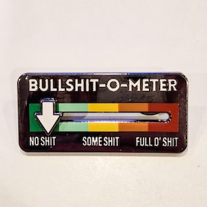 May include: A rectangular metal enamel pin featuring the text BULLSHIT-O-METER at the top. Below, a sliding scale transitions from green to yellow to red, labeled NO SHIT, SOME SHIT, and FULL O' SHIT. A white arrow points to the green section.