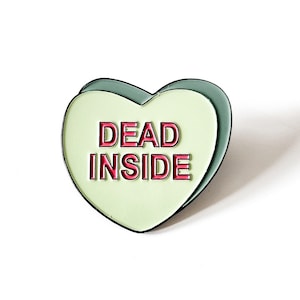 May include: A green heart-shaped pin with the words "DEAD INSIDE" in red letters.