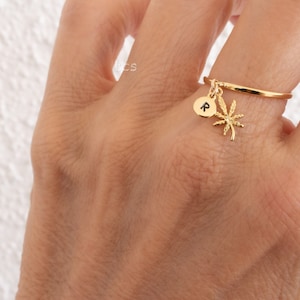 May include: Gold ring with a palm tree charm and a small disc charm with the letter 'R' on it.